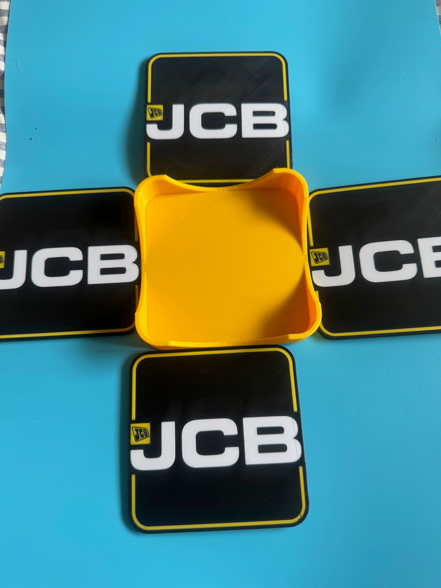 Yellow container surrounded by JCB branded black mats on a blue background